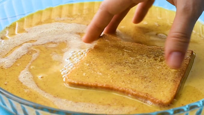 dipping a slice of bread into the egg custard for simple french toast