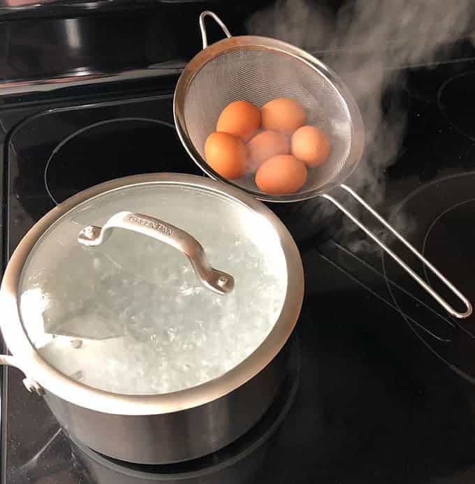 pot of boiling water and a mesh strainer filled with eggs to boil