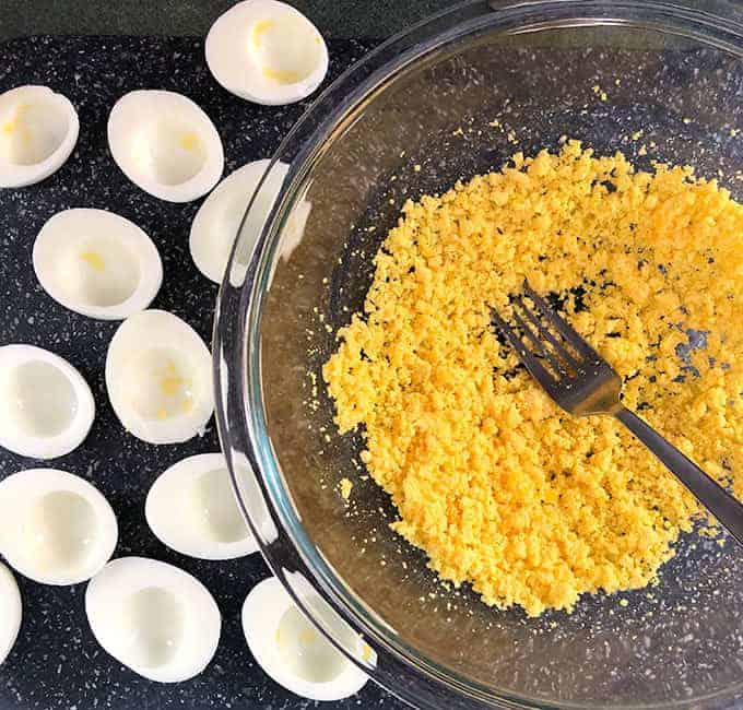 Hard boiled eggs cut in half with the yolks removed and placed in a bowl and mashed with a fork