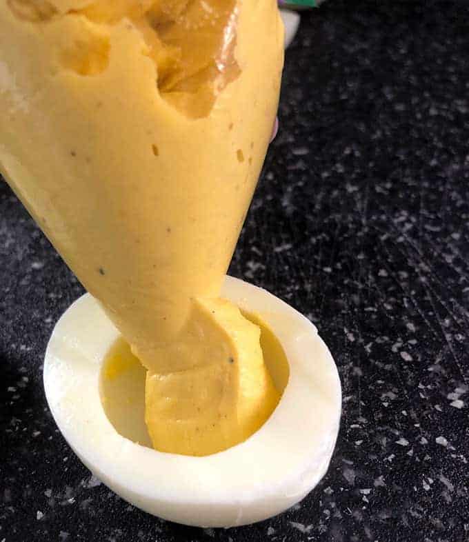 Piping the deviled egg filling into a hard boiled egg white for the best deviled egg recipe