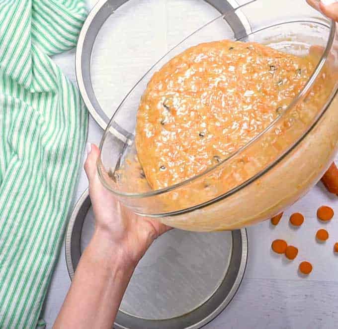 Pouring carrot cake ingredients into 2 cake pans for baking
