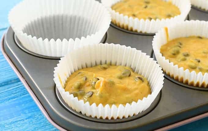 Pumpkin muffin batter in a muffin tin with muffin cup liners