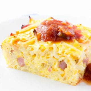 Slice of breakfast casserole with hash browns, ham, and cheese with salsa on top