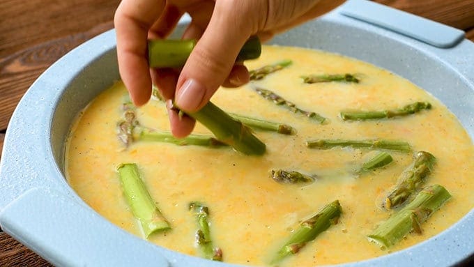 Adding chopped asparagus to a pie plate with ham and cheese quiche ingredients