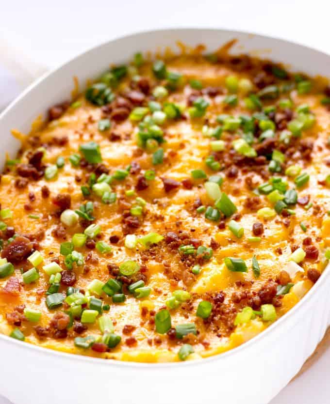 Loaded mashed potato casserole topped with cheddar, green onions, and bacon bits