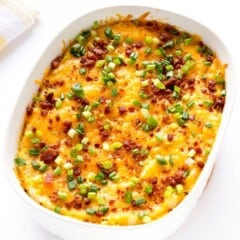 Loaded mashed potato casserole topped with cheese, green onions, and bacon in a white serving bowl