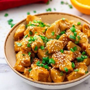 Mandarin chicken in a bowl topped with sesame seeds and sliced green onions