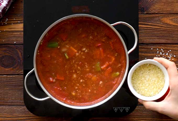 Adding uncooked rice to a pot of stuffed pepper soup