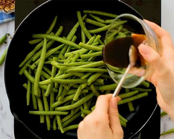 Fresh green beans in a large skillet with Asian sauce being poured over them