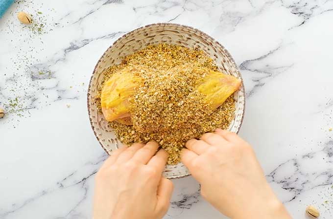 Chicken breast being coated in a mixture of chopped pistachios and Panko bread crumbs