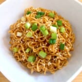 Sesame Peanut Butter Noodles in a white bowl topped with sesame seeds and sliced green onions