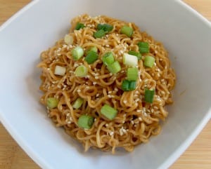 white bowl full of sesame peanut noodles topped with green onions