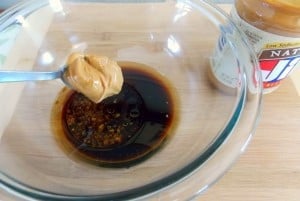 spoon full of peanut butter going into a bowl of soy sauce