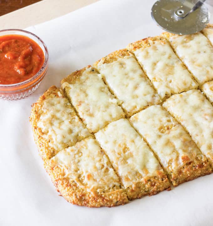 sliced Quinoa Crust on a cutting board next to a bowl of marinara sauce