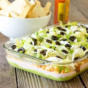 casserole dish full of 7 Layer Chicken Taco Dip with tortilla chips in the background