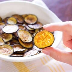 Salt and Vinegar Zucchini Chips in a white bowl and one being held up