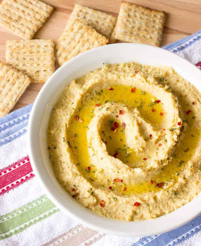 Simple Hummus Without Tahini in a white bowl with crackers on the side