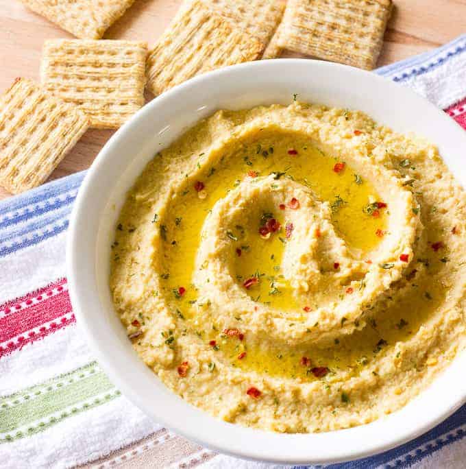 Simple Hummus Without Tahini in a white bowl with crackers on the side