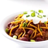 bowl of homemade chili with maple and bourbon topped with cheese, sour cream, and green onions