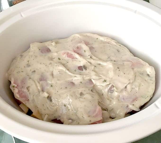 Crock Pot full of Pork Chops Potatoes & Onions covered in mushroom soup