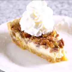 slice of Cheesecake Stuffed Pecan Pie with whipped cream on a white plate