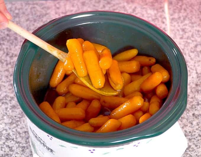 spoon full of Cinnamon Brown Sugar Carrots coming out of a crock pot