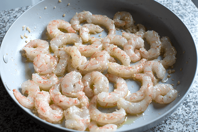 uncooked jumbo shrimp in a skillet with garlic and olive oil