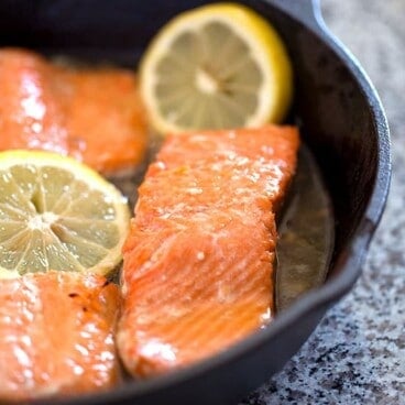 Cooked salmon in a cast iron skillet with honey and lemon slices