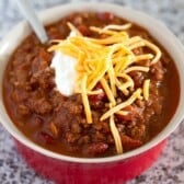 The best classic chili recipe in a red bowl topped with cheddar cheese and sour cream