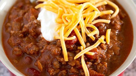 The best classic chili recipe in a red bowl topped with cheddar cheese and sour cream