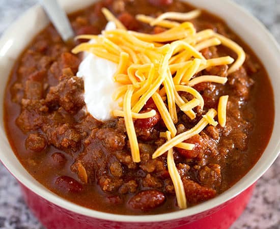 The best classic chili recipe in a red bowl topped with cheddar cheese and sour cream