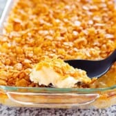 serving spoon going into a baking dish full of cheesy potato casserole with corn flake topping