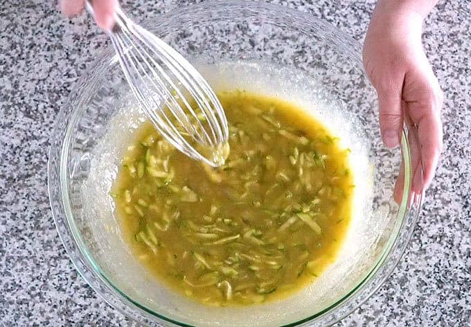 Whisking grated zucchini, sugar, applesauce, oil, brown sugar, and vanilla in a bowl