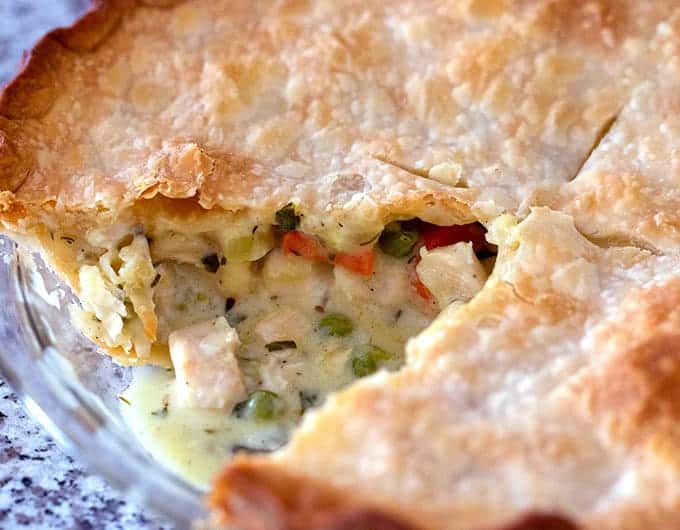 Homemade chicken pot pie in a pie plate with one piece taken out showing the creamy filling