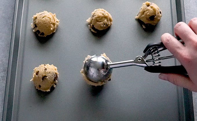 Scoop dropping chocolate chip cookie dough onto a baking sheet