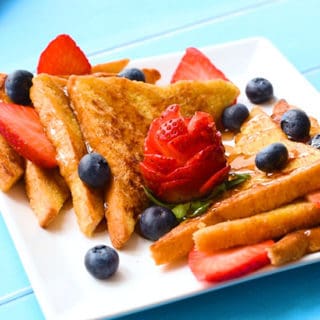 The best classic french toast recipe with pieces sliced on a plate with maple syrup, strawberries and blueberries