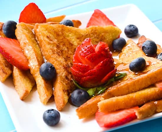 The best classic french toast recipe with pieces sliced on a plate with maple syrup, strawberries and blueberries