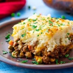 A piece of the best shepherd's pie on a plate with layers of cottage pie beef and vegetable gravy topped with parmesan cheese mashed potatoes