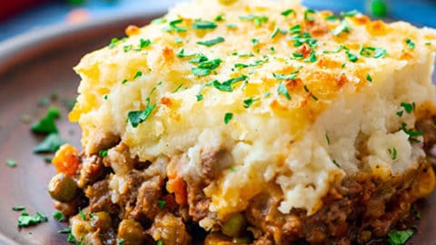 A piece of the best shepherd's pie on a plate with layers of cottage pie beef and vegetable gravy topped with parmesan cheese mashed potatoes