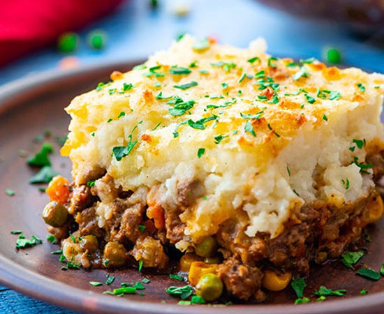 A piece of the best shepherd's pie on a plate with layers of cottage pie beef and vegetable gravy topped with parmesan cheese mashed potatoes