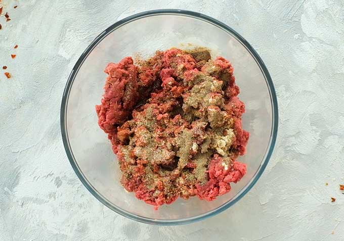 A mixing bowl full of ground beef, Worcestershire sauce, seasoning salt, garlic powder, and pepper for the best hamburger recipe