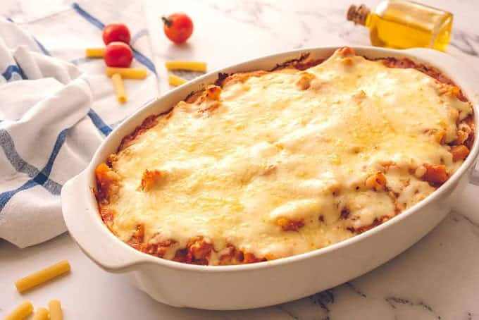 Large baking dish full of baked ziti covered in cheese