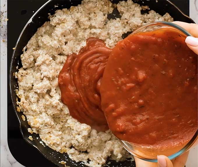 pouring pasta sauce into a skillet with Italian sausage and ricotta cheese