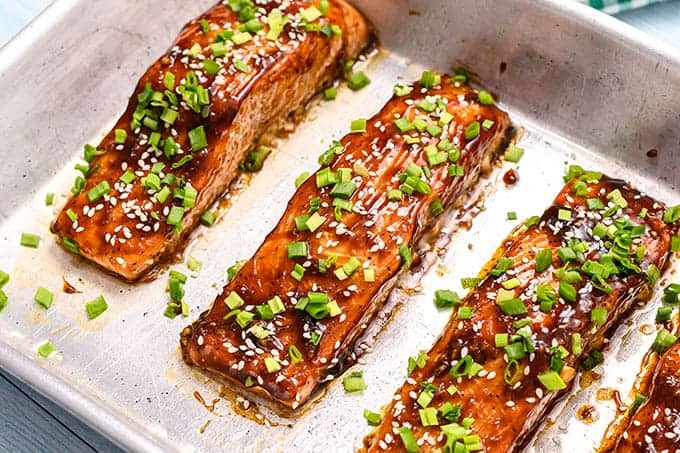 baking dish full of baked salmon filets coated in teriyaki sauce, sesame seeds, and sliced green onions