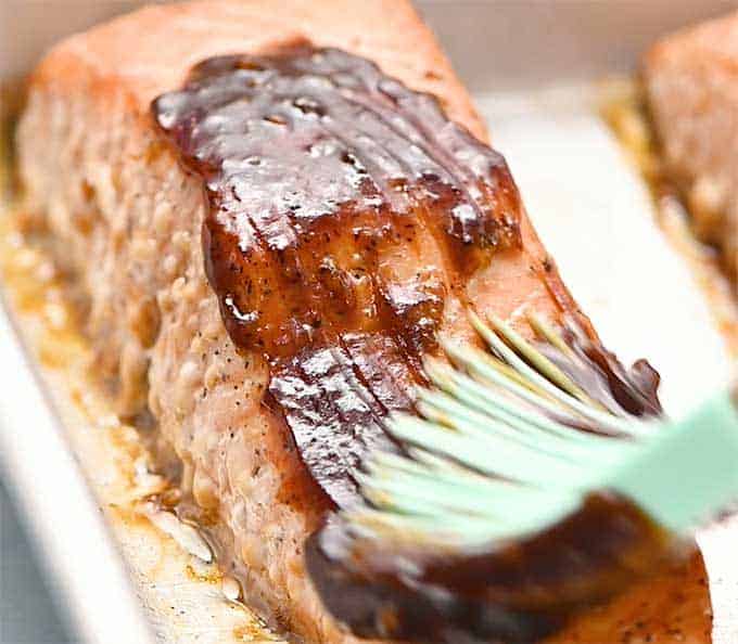 Baked salmon fillet being brushed with thick teriyaki glaze