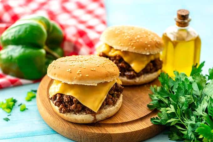 Two sloppy Joe sandwiches with cheese on a cutting board.