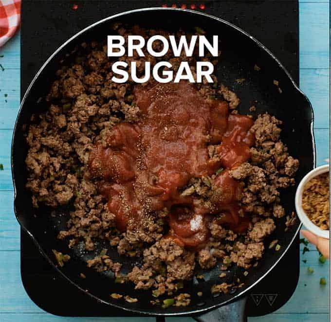 Skillet full of cooked ground beef, peppers, onions, tomato sauce, and brown sugar.