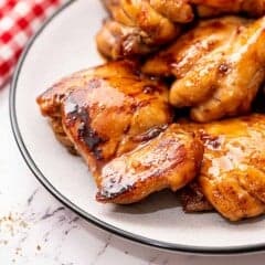 cooked boneless skinless chicken thighs coated in teriyaki glaze piled on a white plate