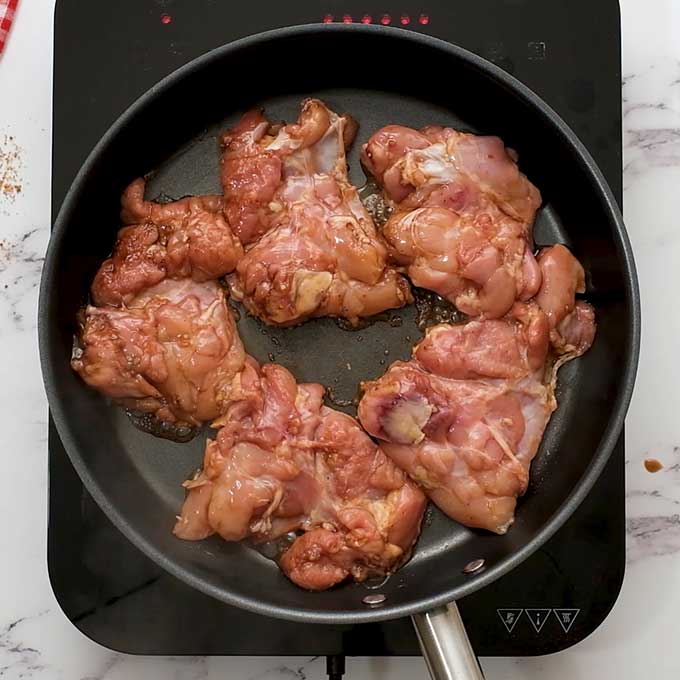 chicken thighs being cooked in a large skillet