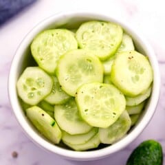 peeled, sliced, vinegar marinated cucumbers in a white bowl